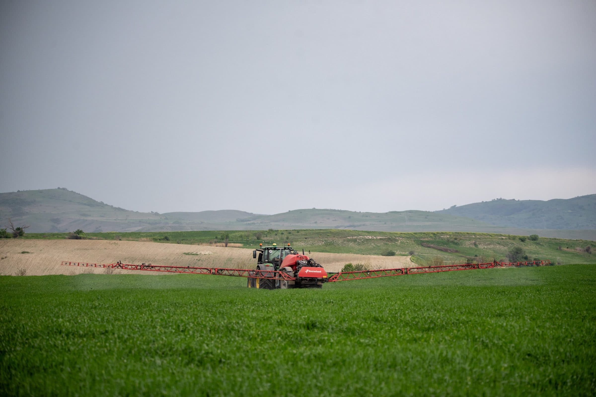 Tractor with a wide crop-sprayer boom working a green field