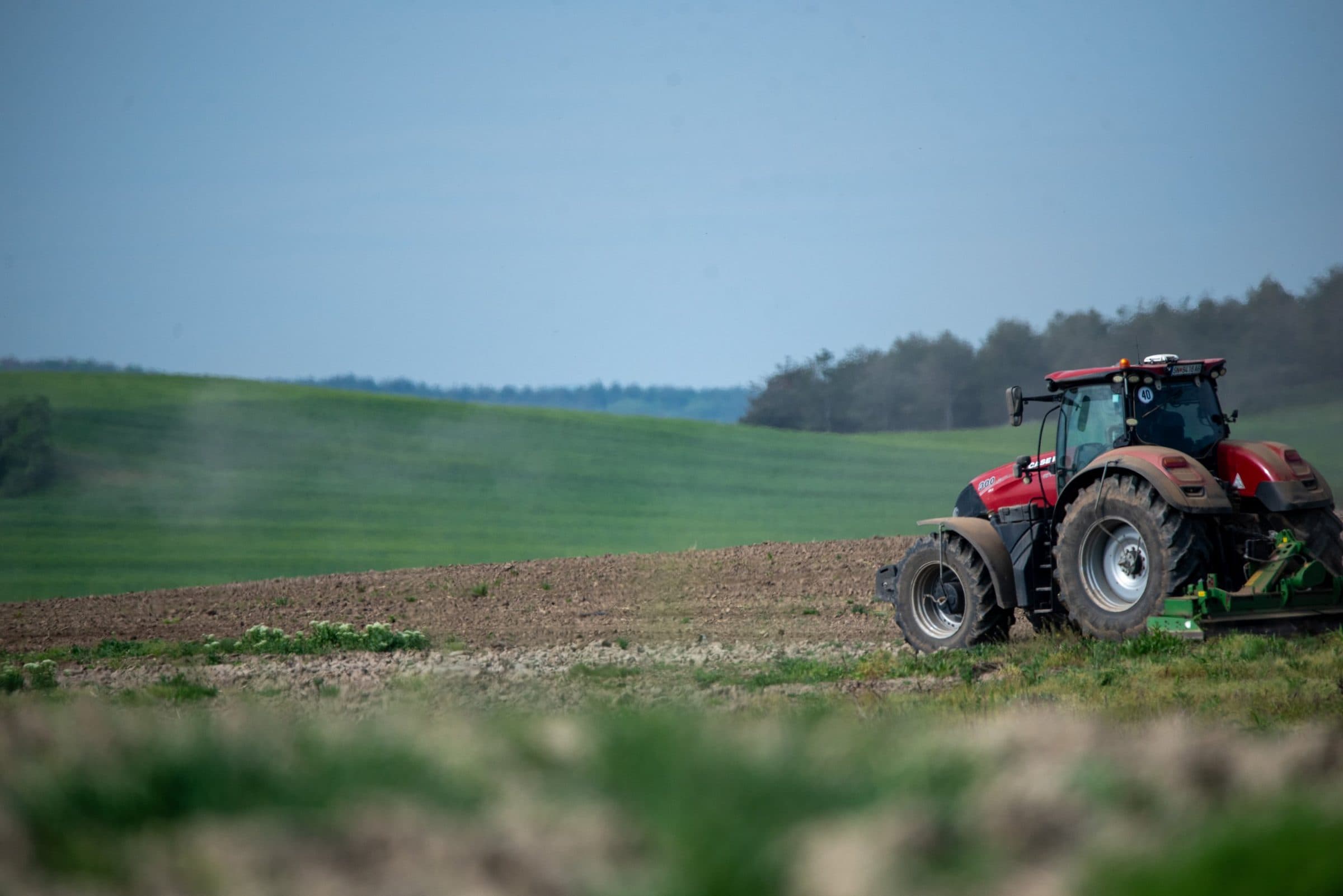 Tractor preparing soil at the edge of a green field